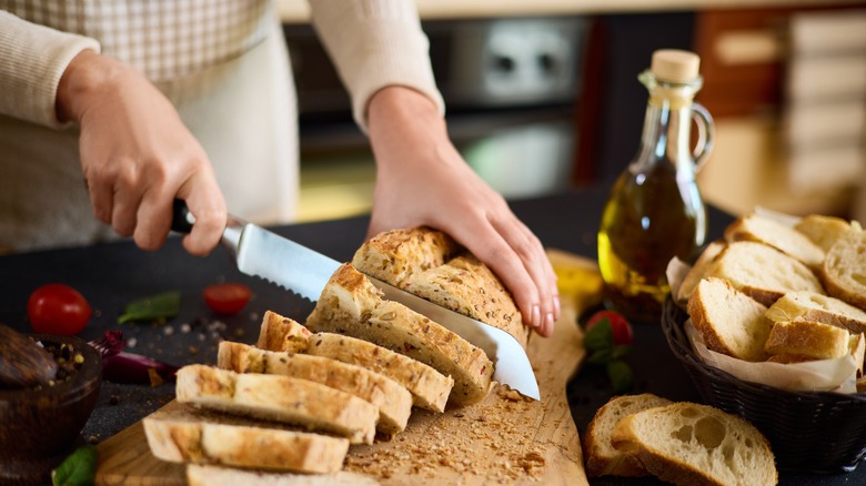 Person slicing a loaf of bread next to a bottle of olive oil