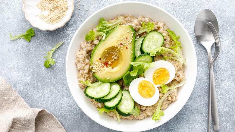 Bowl of savory oatmeal with hard boiled egg, avocado, cucumber and lettuce