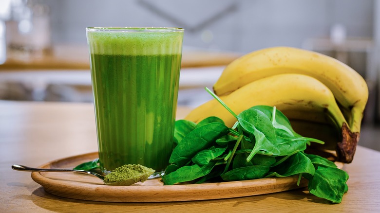 Green smoothie next to spoonful of matcha, spinach leaves, and bananas