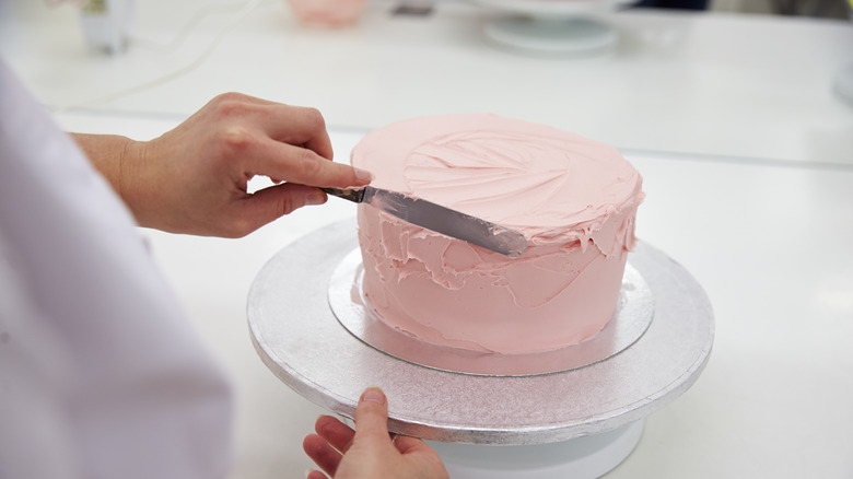 Person icing pink cake