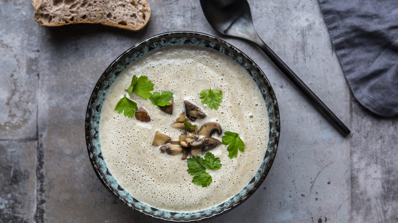 A black bowl of cream of mushroom soup sits beside crust of brown bread