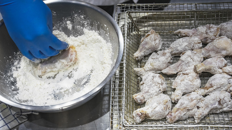 A hand dipping fried chicken in batter