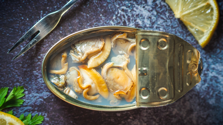 Canned clams in an opened tin next to a fork and lemon slice