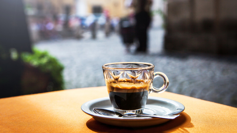 A small mug of espresso rests on an outdoor table at an Italian cafe