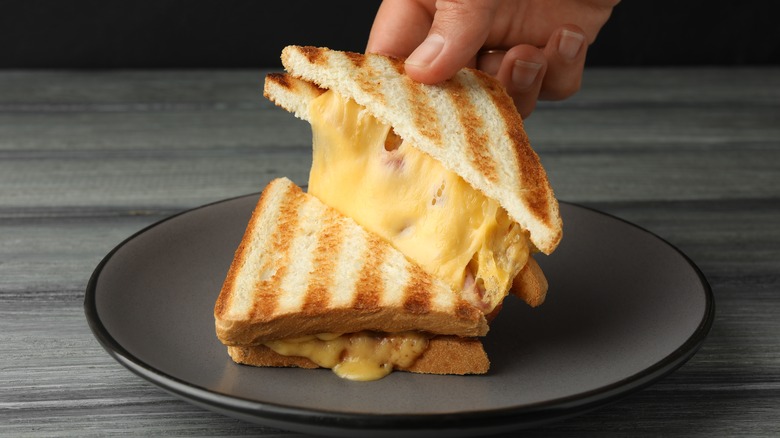 One slice of a diagonally cut grilled cheese is being pulled by a fair skinned hand