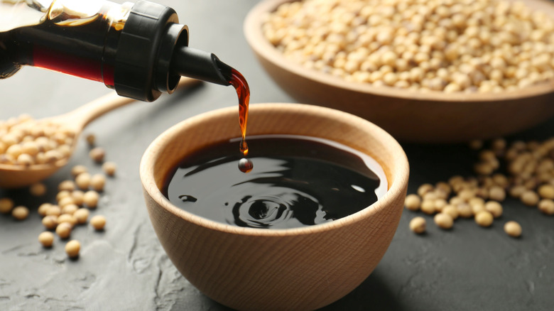 Soy sauce being poured from a beaker into a green ceramic bowl on a table with a white tablecloth