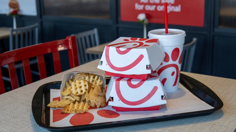 A tray of Chick-fil-A food on a table in the restaurant, including waffle fries, two sandwich boxes, and a soda