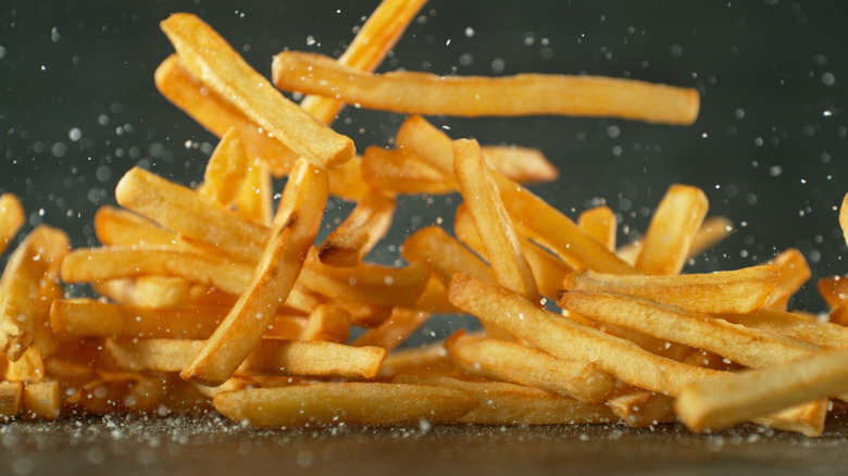 Salted golden french fries falling onto a table