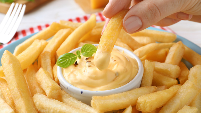 Fingers dip a french fry into a yellow sauce with an herb garnish