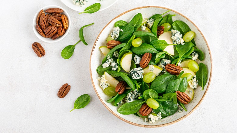 Spinach salad with pecans, apples, grapes, and blue cheese in white bowl