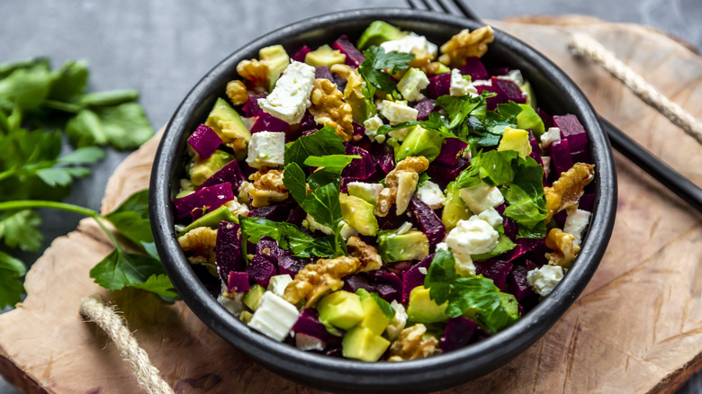 Salad with greens, walnuts, avocado, beets, and feta in black bowl