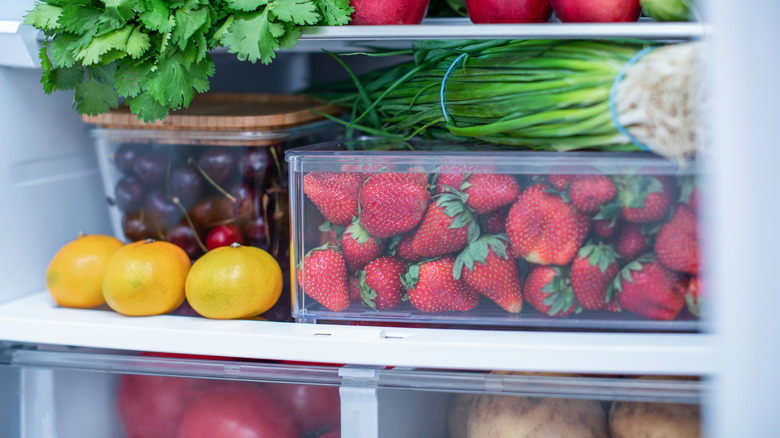 Strawberries in a container and other vegetables in a fridge