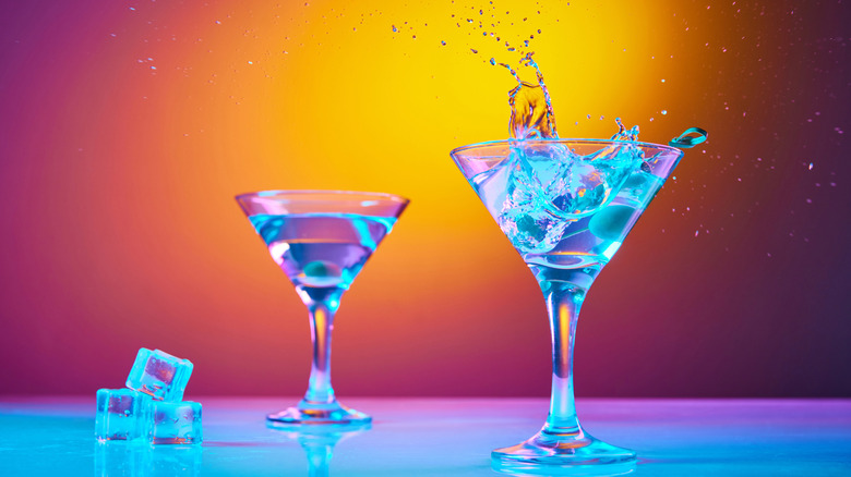 Dry martini seems to glow as an olive splashes and spills alcohol out of the glass