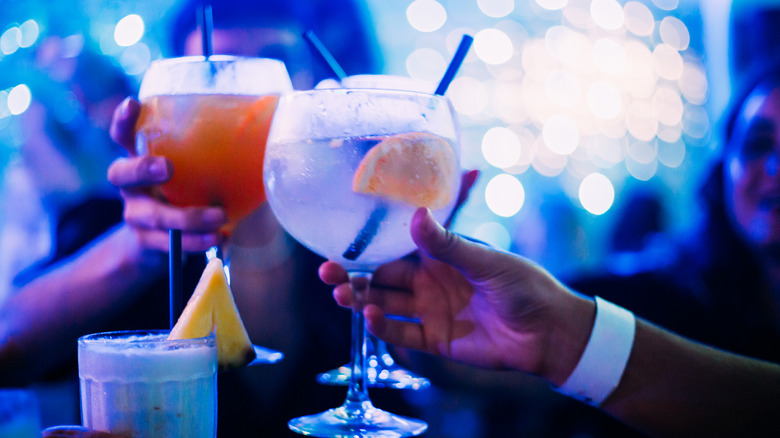 Group of people at a nightclub drinking cocktails on a neon light and sparkle background