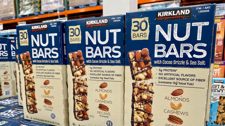 Three blue and cream boxes of nut bars with a picture of the bar on front, surrounded by other boxes