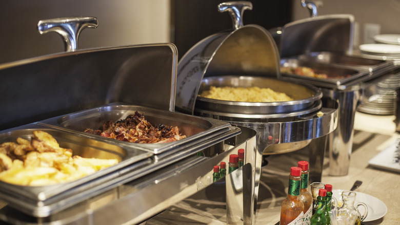 Metal serving dishes filled with potatoes, bacon, eggs, and other food items at a deluxe continental breakfast