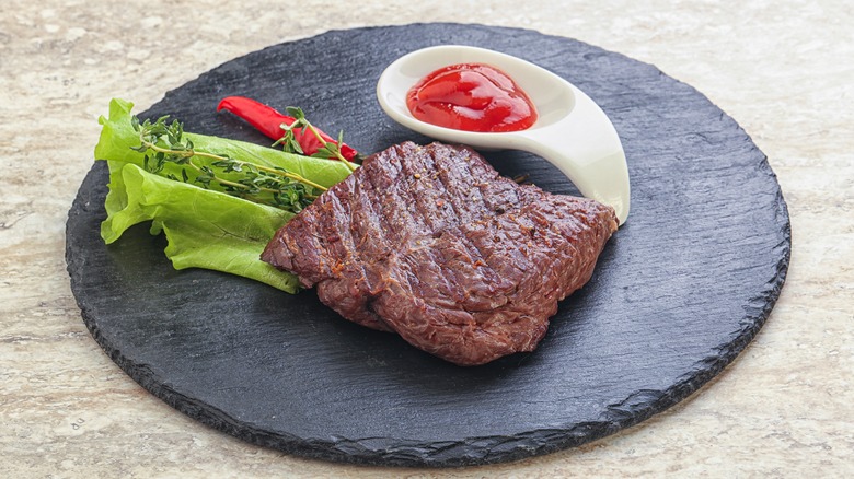 Steak on round black plate with ketchup