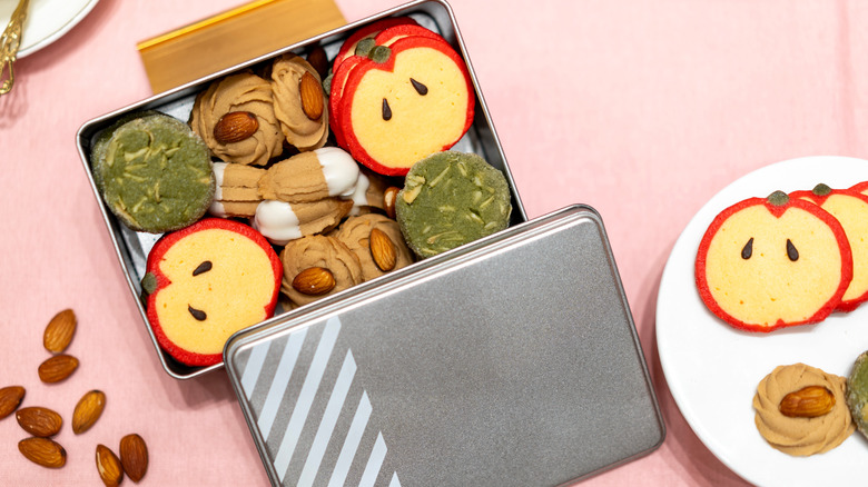 A cookie tin filled with sugar cookies and almond swirls on a pink table