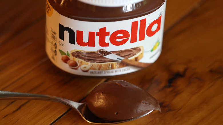 A spoonful of Nutella sits next to its jar