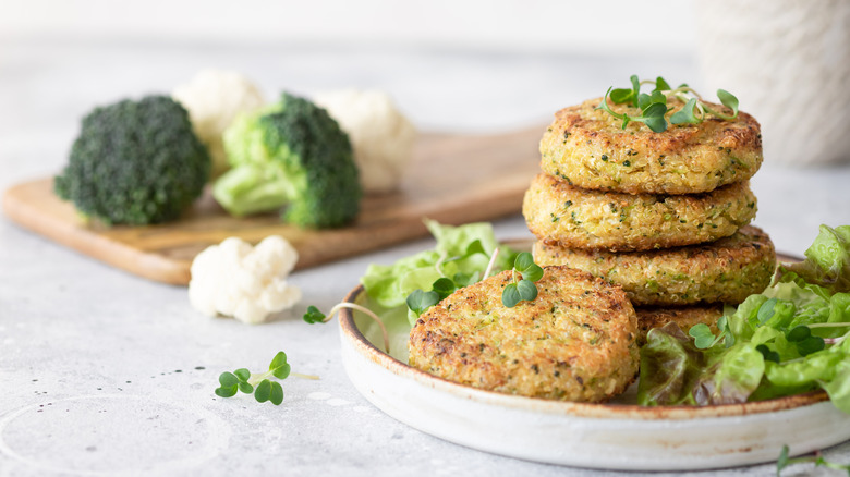 Veggie patties stocked on a white plate with broccoli and cauliflower in the background.