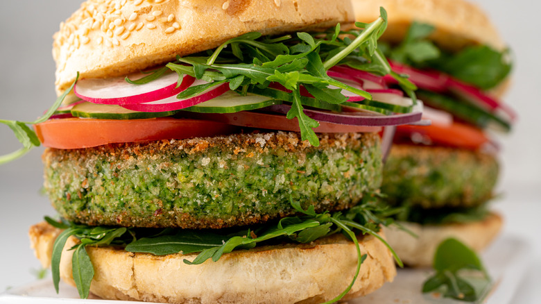 Veggie burger on a sesame seed bon with tomatoes, greens, and onion.