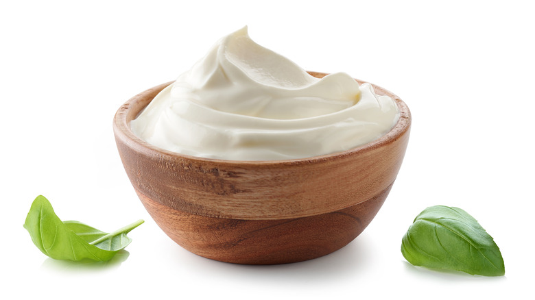 Wooden bowl of sour cream with basil leaves