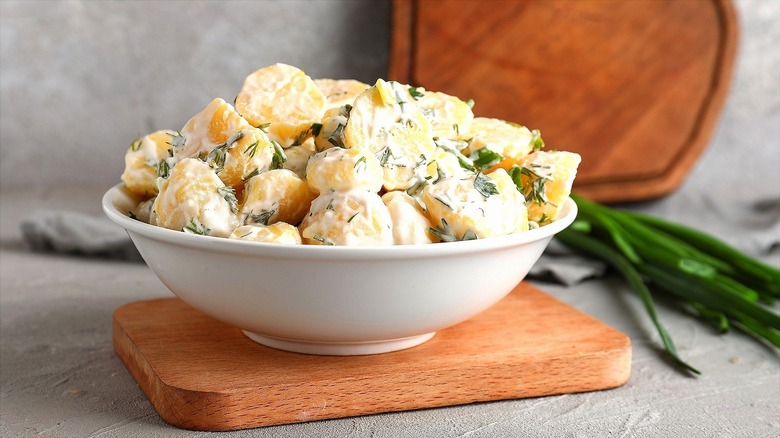 Bowl of creamy potato salad with herbs on a wooden board