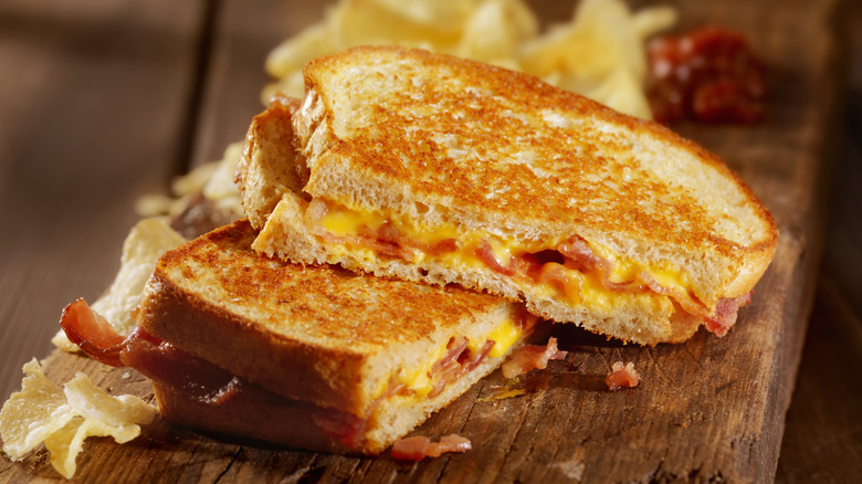 Grilled cheese sandwich with bacon, and potato chips on the side. All on a wooden table.