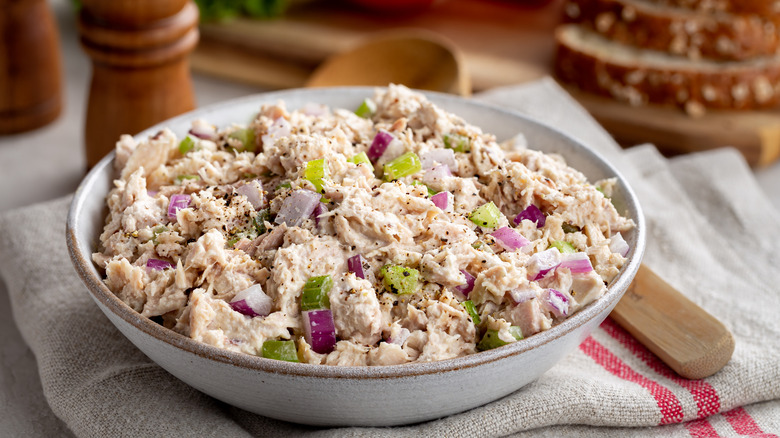 A bowl of tuna salad with red onions and celery sits next to a wooden spoon