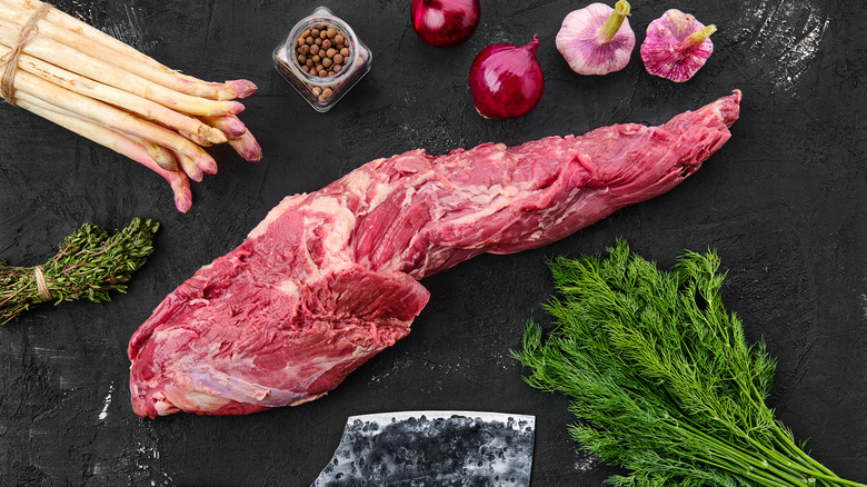 Untrimmed beef tenderloin surrounded by seasonings