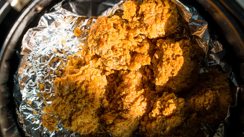 An air fryer basket lined with foil and fried chicken on top