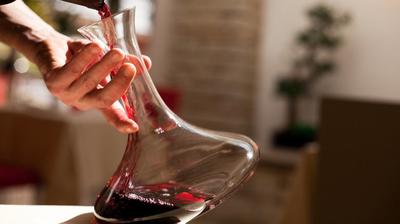 A person pours red wine into a wide-bottomed decanter