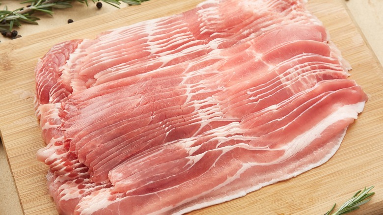 Slab of raw bacon slices on cutting board