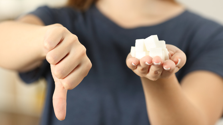 Woman holding sugar cubes makes thumbs down gesture