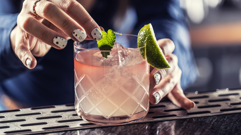 A bartender's hand placing a garnish of lime and mint on top of a margarita with a red wine float