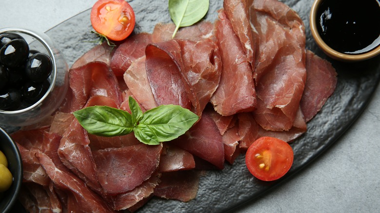 Bresaola on serving platter with tomato and basil leaves
