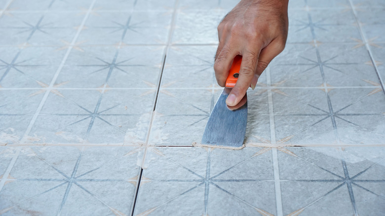 A man's hand installs grout on a tile floor