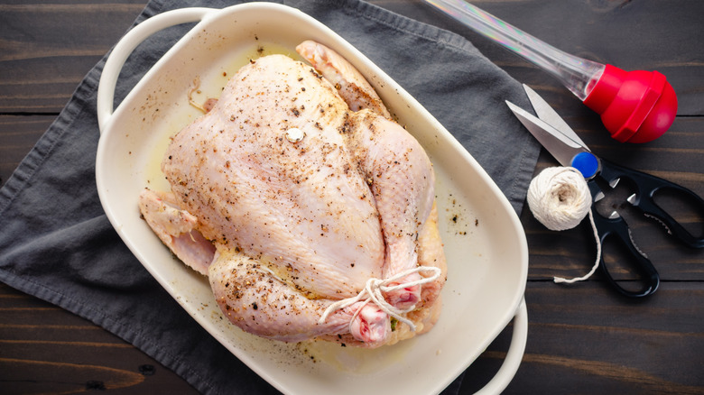 Raw seasoned chicken in a casserole dish on a dark wooden table with rope and scissors