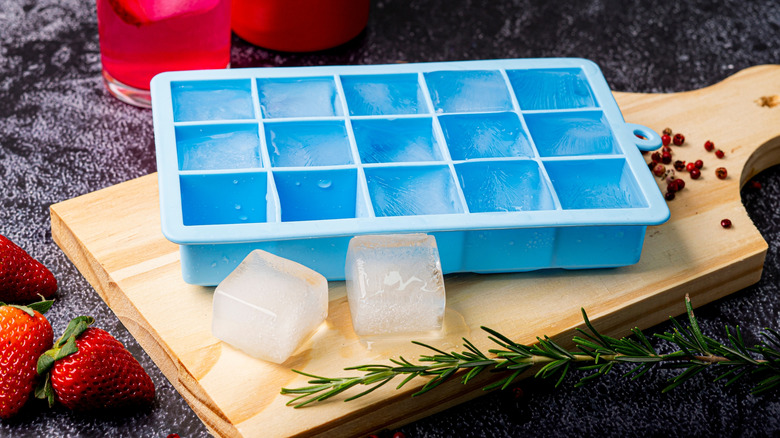 Blue silicone ice mold filled with ice cubes on wooden cutting board