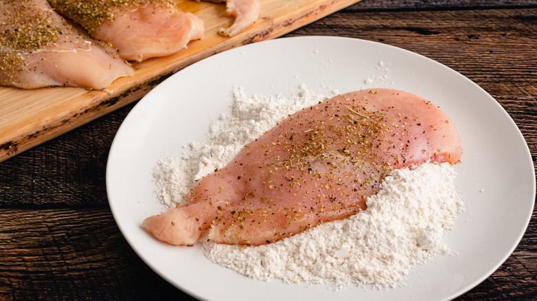 Raw chicken breast sitting on top of pile of flour