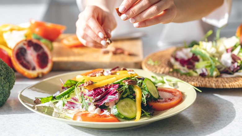 A woman's hands add toppings to a plate of salad