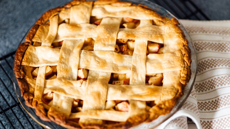 Close up of apple pie on a baking rack with a towel underneath.