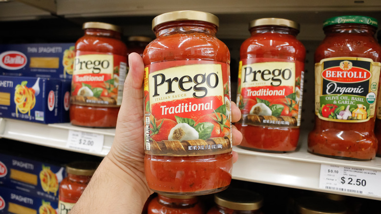 A hand holds a jar of Prego marinara sauce, on display at a grocery store