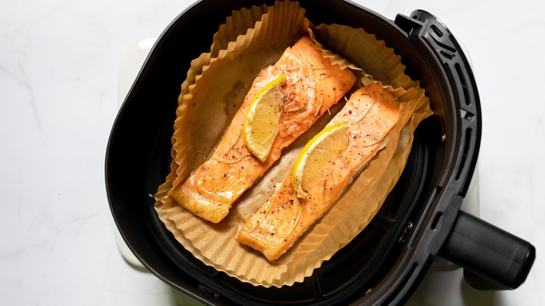 salmon with lemon slices sitting on parchment paper inside air fryer
