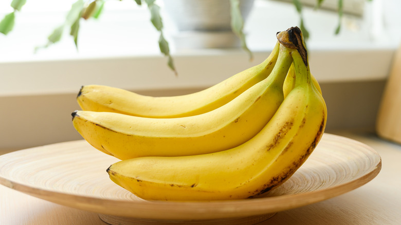 a bunch of ripe bananas on a wooden plate with plant in background