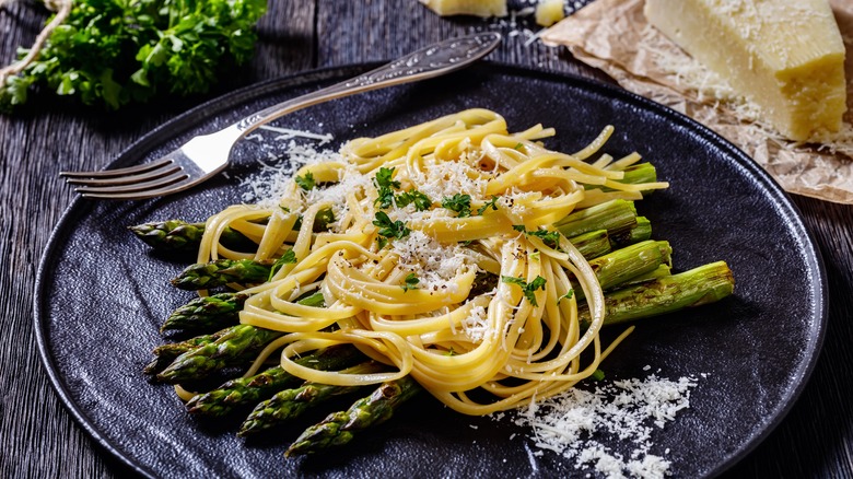 Charred asparagus with pasta noodles and grated cheese on black plate