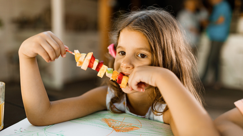 Girl eating a fruit kabob