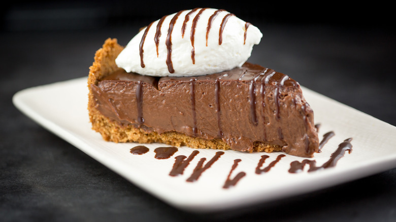 Piece of chocolate cream pie with cream and chocolate drizzle on white square plate