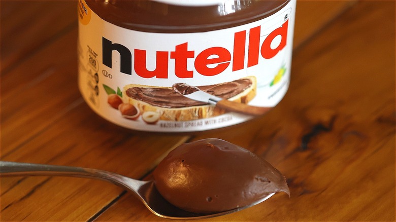 Jar and spoonful of Nutella on wooden surface