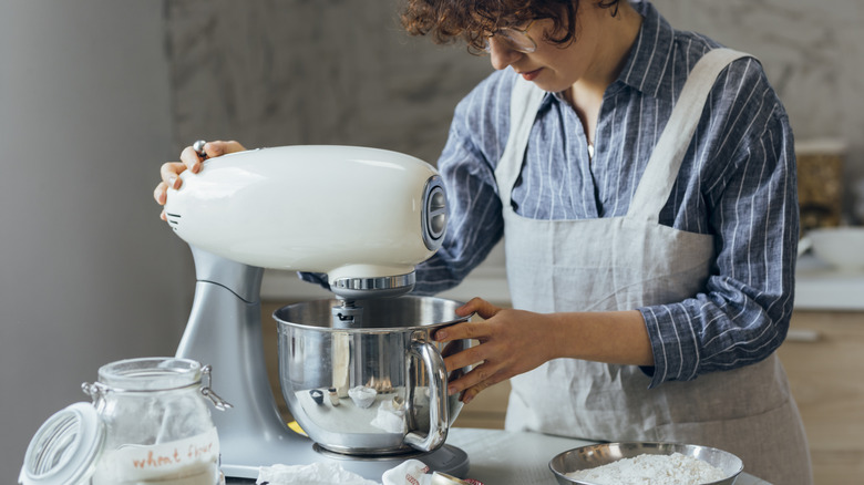 Person with apron and glasses adjusting a stand mixer while preparing a recipe